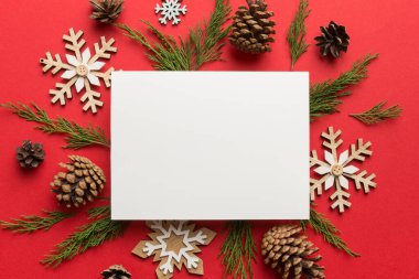 Noel kompozisyonu düzdü. Kare kağıt boş, çam ağacı dalları, renkli arka planda noel süslemeleri. Üst görünüm, metin için boşluk kopyala.