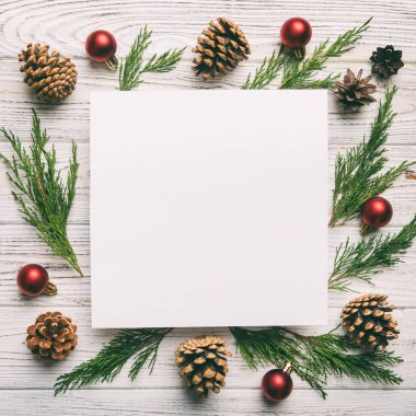Noel kompozisyonu düzdü. Kare kağıt boş, çam ağacı dalları, renkli arka planda noel süslemeleri. Üst görünüm, metin için boşluk kopyala.