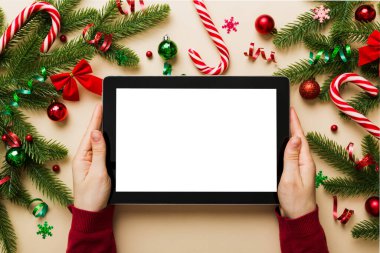 Evden Noel alışverişi, kadın elleri boş beyaz ekranlı tableti tutuyor. Kadın elinde tablet, boş ekran, Noel ağacı ve arka planda hediyeler..