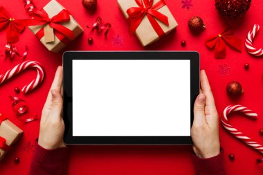 Evden Noel alışverişi, kadın elleri boş beyaz ekranlı tableti tutuyor. Kadın elinde tablet, boş ekran, Noel ağacı ve arka planda hediyeler..