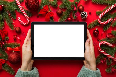 Evden Noel alışverişi, kadın elleri boş beyaz ekranlı tableti tutuyor. Kadın elinde tablet, boş ekran, Noel ağacı ve arka planda hediyeler..