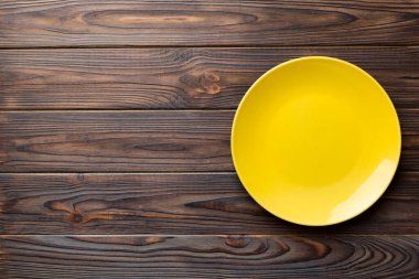 Ahşap arka planda boş sarı tabağın üst görüntüsü. Tasarımın için boş boşluk.