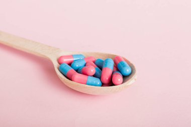 Vitamin capsules in a spoon on a colored background. Pills served as a healthy meal. Red soft gel vitamin supplement capsules on spoon.