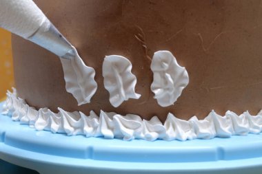 Elinde pasta poşeti olan bir kadın pasta şefi ev mutfağında pastaya krema sıkıyor. Fırın mutfağında çalışan profesyonel bir şef. Yemek pişirme, yemek pişirme, ev yemeği..