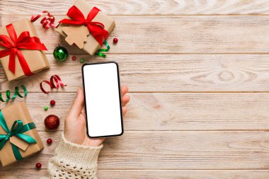 Mesaj atmak için yeri olan bir Noel modeli. Noel reklamı, uygulama şablonu. Masa arkasında boş ekran olan el ele tutuşan telefon. Mutlu yıllar ve Xmas Flat.