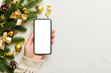 Mesaj atmak için yeri olan bir Noel modeli. Noel reklamı, uygulama şablonu. Masa arkasında boş ekran olan el ele tutuşan telefon. Mutlu yıllar ve Xmas Flat.