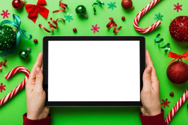 Evden Noel alışverişi, kadın elleri boş beyaz ekranlı tableti tutuyor. Kadın elinde tablet, boş ekran, Noel ağacı ve arka planda hediyeler..