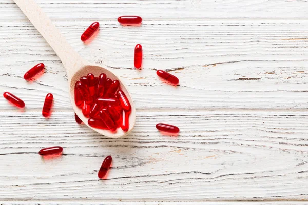 Vitamin capsules in a spoon on a colored background. Pills served as a healthy meal. Red soft gel vitamin supplement capsules on spoon.