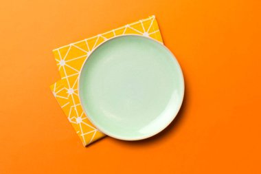 Renkli arka planda üst görünüm yiyecek için masa örtüsünün üzerinde boş yuvarlak yeşil tabak. Tasarımınız için boşluk olan peçeteye boş tabak.