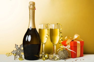 Champagne bottle with confetti, glasses and christmas decor on colored holiday background. Flat lay New Year decorations.