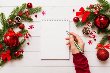 Noel 'i yazmak için bir kadın not defterine Xmas dekorasyonlu renkli arkaplan çiziyor.