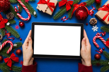 Evden Noel alışverişi, kadın elleri boş beyaz ekranlı tableti tutuyor. Kadın elinde tablet, boş ekran, Noel ağacı ve arka planda hediyeler..
