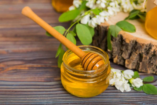 Sweet honey jar surrounded spring acacia blossoms. Honey flows from a spoon in a jar. jars of clear fresh acacia honey on wooden background.