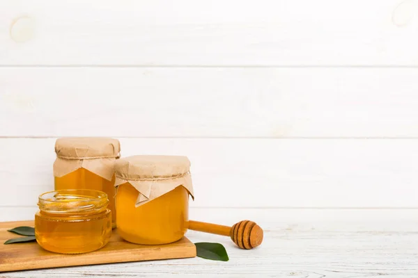 Honey in jar with leaves and honey dipper on colored background top view with copy text.