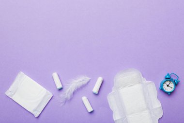 Alarm saatini hijyenik kadın tamponları ve regl pedleri ile çalıyor. Tıbbi konsept kadın kritik günler ve regl dönemi. Kadın günlük hijyen. Boşluğu kopyala.