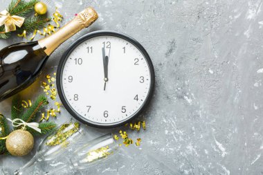 New year celebration concept with a bottle of champagne and two glasses toasting. Christmas gift box, alarm clock and fir tree branch on colored table. Top view Copy space.