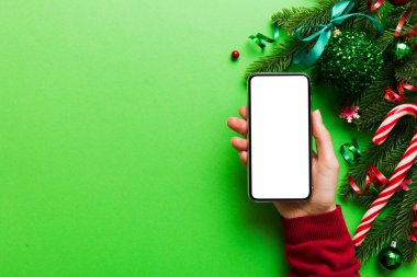Mesaj atmak için yeri olan bir Noel modeli. Noel reklamı, uygulama şablonu. Masa arkasında boş ekran olan el ele tutuşan telefon. Mutlu yıllar ve Xmas Flat.