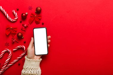 Mesaj atmak için yeri olan bir Noel modeli. Noel reklamı, uygulama şablonu. Masa arkasında boş ekran olan el ele tutuşan telefon. Mutlu yıllar ve Xmas Flat.