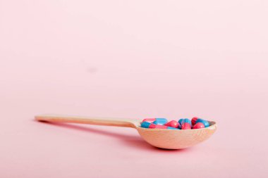 Vitamin capsules in a spoon on a colored background. Pills served as a healthy meal. Red soft gel vitamin supplement capsules on spoon.