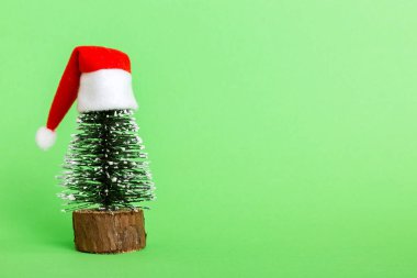 One small Christmas tree with santa hat on colored background. new year decoration with copy space.