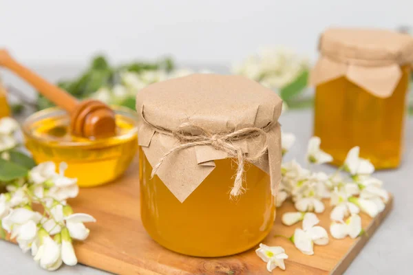 Sweet honey jar surrounded spring acacia blossoms. Honey flows from a spoon in a jar. jars of clear fresh acacia honey on wooden background.