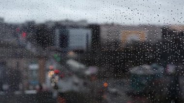 Yağmurlu bir günde şehrin bulanık pencere manzarası. Pencereye su damlıyor, soyut bir arkaplan. Pencerenin dışında yağmur yağıyor. Yağmurdan sonra cam üzerinde doğal su damlaları.