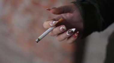 A smoldering cigarette with a filter in a female hand. The concept of the harm of smoking.
