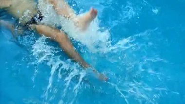Boy splashing in water with his feet in the pool. Summer vacation concept. Water procedures in the summer in the pool.