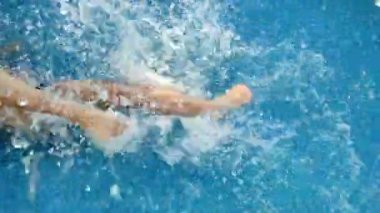 Boy splashing in water with his feet in the pool. Summer vacation concept. Water procedures in the summer in the pool.