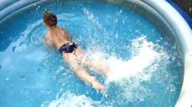 Boy lying on stomach splashing in water with his feet in the pool. Summer vacation concept. Water procedures in the summer in the pool.