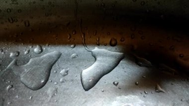 Close-up of water drops slowly flowing down a metal surface. Drops of water on silver metal.