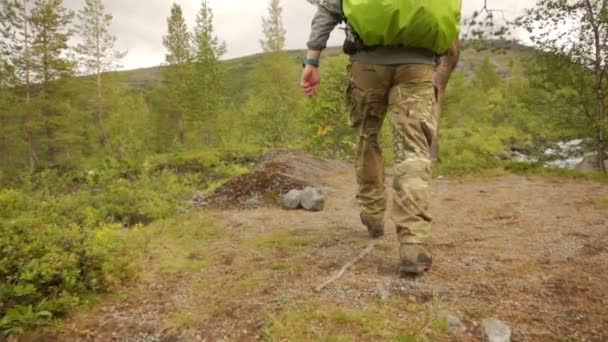 Un viajero sale a la orilla de un río de montaña con una gran mochila verde — Vídeos de Stock