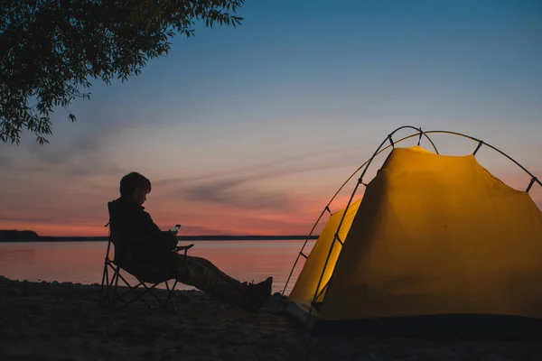 여행자는 빛나는 천막 근처에 있는 캠핑용 의자에 앉아 있다 — 스톡 사진