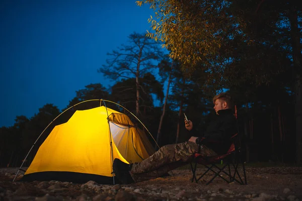 旅行者は輝くテントの近くのキャンプチェアに座っています — ストック写真