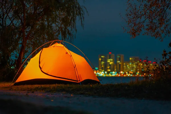 A young guy in jacket sitting inside of orange tent and looking at smartphone — Stock Photo, Image