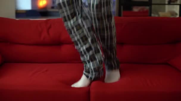 Primer plano de un hombre en pijama a cuadros y calcetines blancos saltando en un sofá rojo — Vídeos de Stock