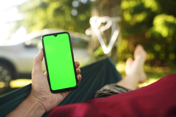 Hamakta dinlenen akıllı telefonlu bir adamın eli.