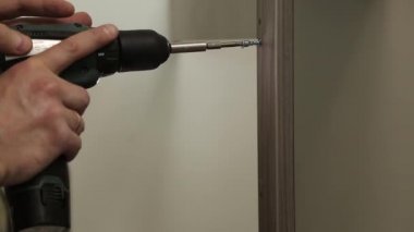 Bir adam elektrikli tornavidayla delik açıyor.