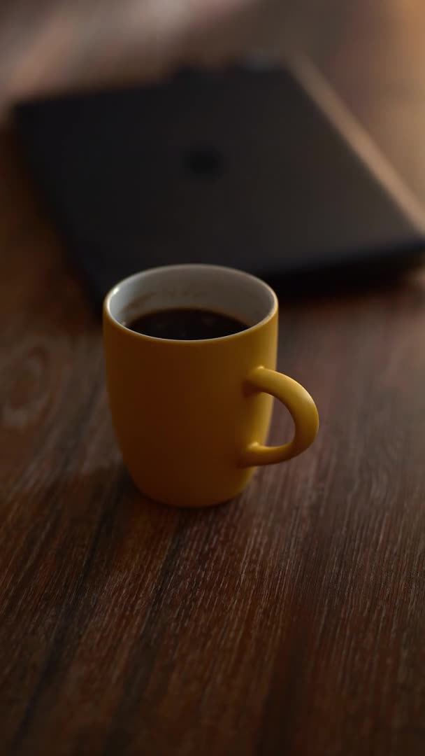 Una taza amarilla de café humeante. Ambiente de trabajo. Una persona trabaja en una computadora portátil en casa — Vídeos de Stock
