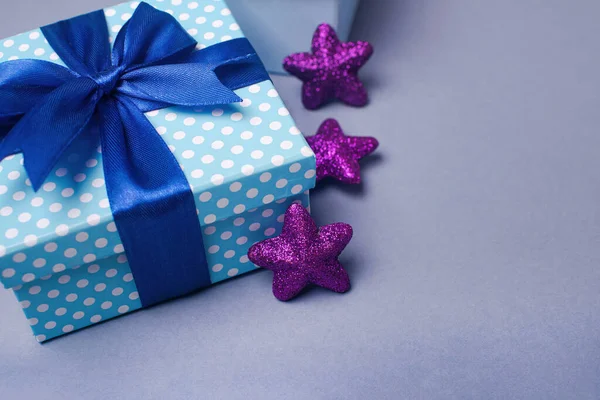 Coffret cadeau bleu avec un arc et des étoiles violettes sur fond gris. Carte de voeux vacances. — Photo