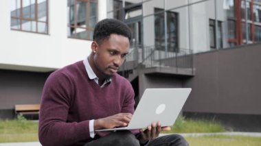 Düşünceli, genç, yakışıklı, serbest çalışan, çimenlerde dizüstü bilgisayar kullanan bir zenci..