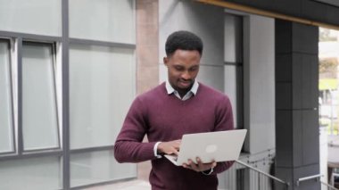 Genç Amerikalı yakışıklı adam dışarıda dizüstü bilgisayarla dolaşıyor.. 