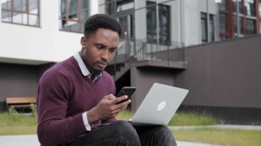 Afro-Amerikalı adam cep telefonunu dizüstü bilgisayara kod girmek için kullanıyor..