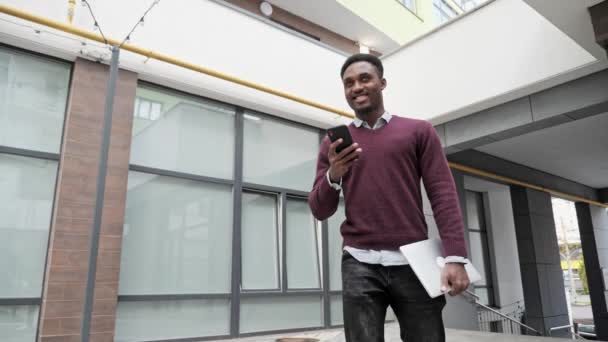 Hombre guapo de piel oscura dando un paseo lento por la ciudad, disfrutando de la conversación. — Vídeo de stock