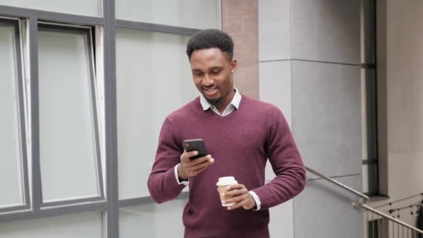 Afro-Amerikaanse Man met behulp van zakelijke app op smart phone wandelen in de stad district. — Stockvideo