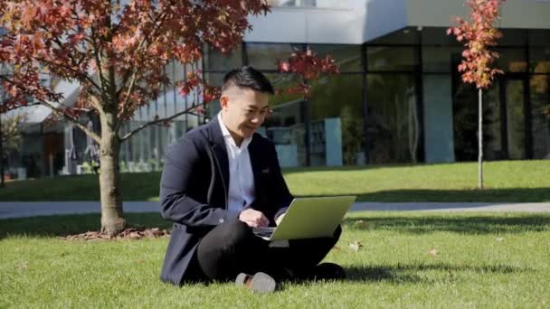 El entrenador chino está enseñando en línea mientras está sentado en la hierba. Conferencia en línea. — Vídeo de stock