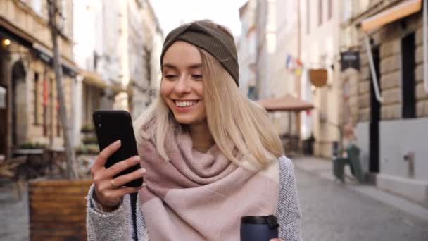 Lächelnd Wunderschöne Blonde mit charmantem Lächeln und blauen Augen, die in der City Street steht, während sie in den sozialen Medien mit modernen Smartphones surft. Attraktive Lady tippt Nachricht online. — Stockvideo