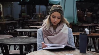 Güzel sarışın kız boş bir restoranın terasında oturup kitap okuyor. Palto giymiş güzel bir kız roman okuyor ve bir sonbahar günü açık havada olmaktan hoşlanıyor.. 