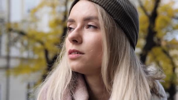 Portretgezicht. Close-up zicht op mooi blond meisje met blauwe ogen op een achtergrond van oude stadsgebouwen en bomen met gele bladeren. Meisje Gezicht Buiten. Natuurlijke vrouwelijke schoonheid. — Stockvideo