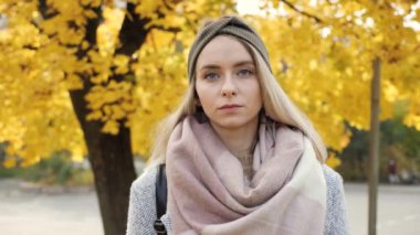 Sonbahar sarı ağaç yapraklarının arka planında mavi gözlü güzel sarışın kızın yakın görüntüsü. Kendine güvenen kız yüzü, kameraya bakan kadın. Doğal Kadın Güzelliği.